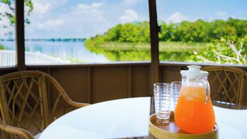 A table with a pitcher of orange juice and glasses, overlooking a body of water and greenery.