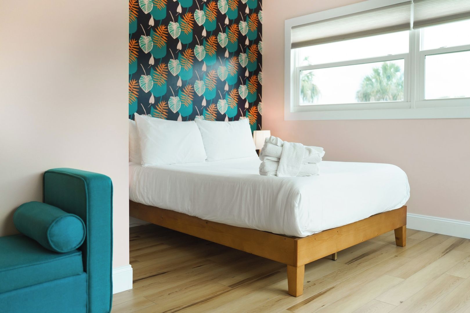 A neatly made bed with white linens, a teal armchair, and a patterned wall.