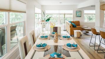 A modern dining area with a long table set for a meal, surrounded by chairs, a sofa, and a kitchen area.