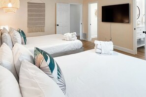 Habitación de hotel con dos camas, televisión y baño visible a través de una puerta abierta.