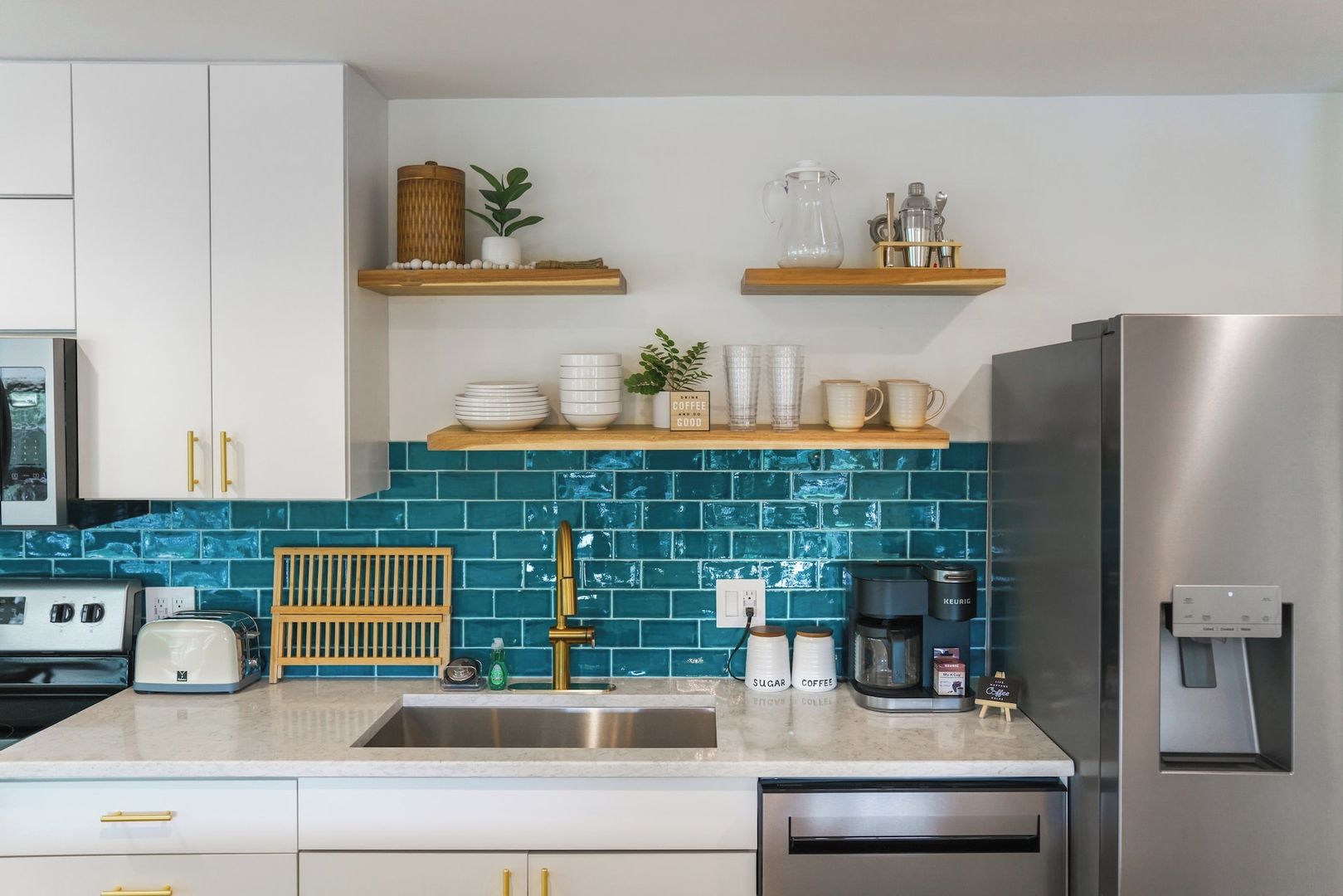 A kitchen with a stainless steel refrigerator, a coffee maker, and a sink with a wooden rack.