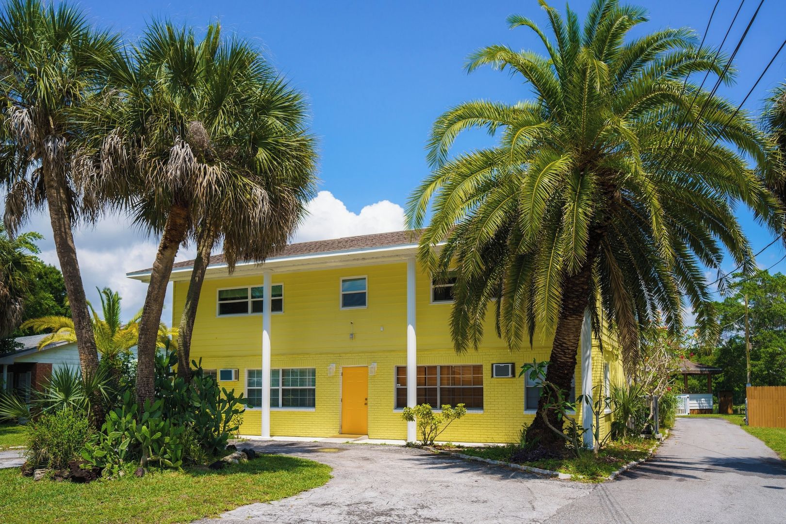 A two-story yellow building with a central entrance, surrounded by palm trees and a clear sky.