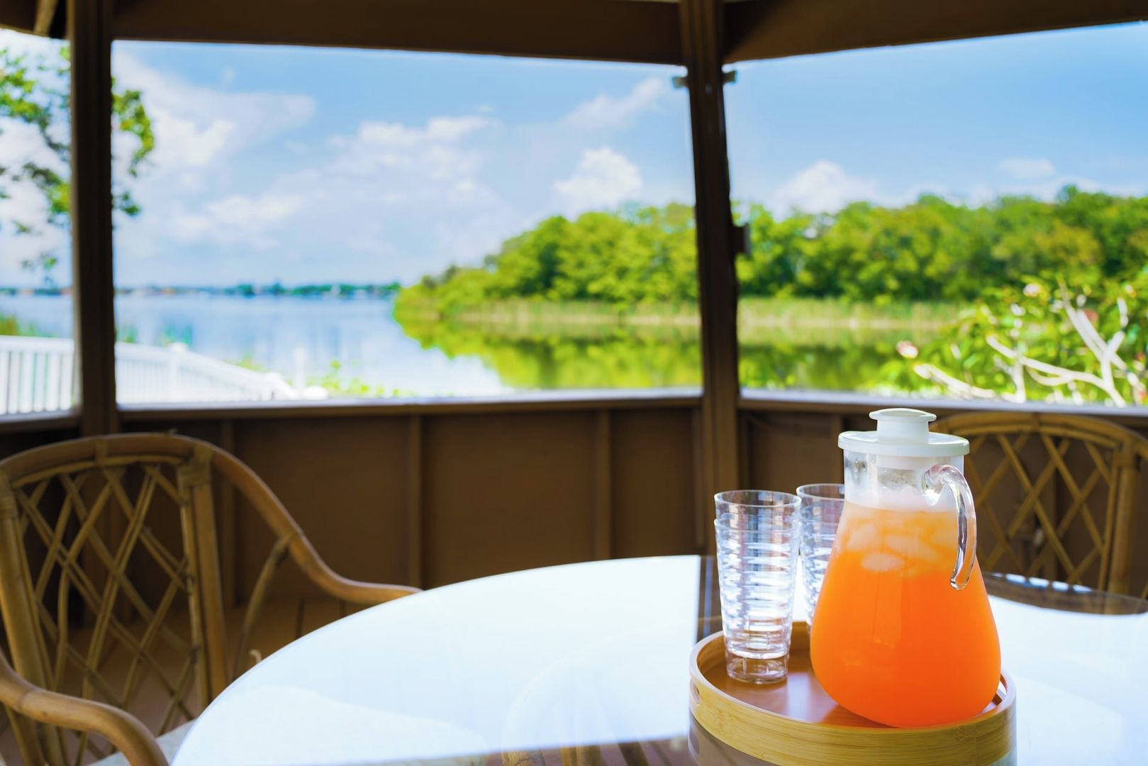 A table with a pitcher of orange juice and glasses, overlooking a body of water and greenery.