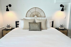 Una cama bien hecha con cabecera, dos mesitas de noche con lámparas y objetos decorativos con forma de estrella en las mesillas.