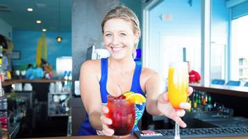 A person holding two drinks at a bar with a modern interior and a view of the city through large windows.