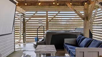 A covered outdoor seating area with a hot tub, wooden beams, and string lights.