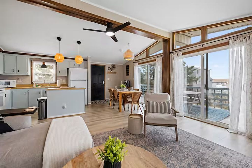 A spacious living area with a dining table, a sofa, and a large window with curtains.