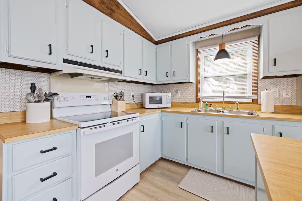 A kitchen with white cabinets, a microwave, a stove, and wooden countertops.