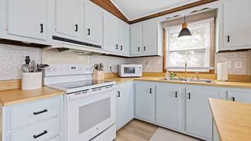 A kitchen with white cabinets, a microwave, a stove, and wooden countertops.