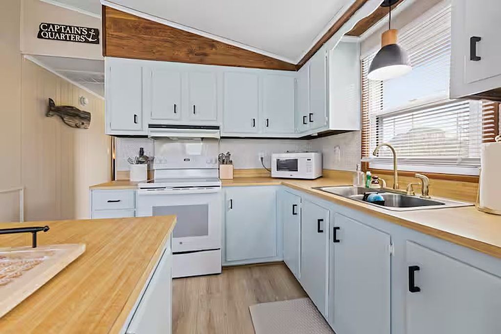 A kitchen with white cabinets, a microwave, a sink, and a wooden countertop.