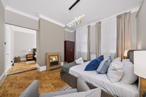 A modern hotel room with a large bed, a wooden floor, a fireplace, and a view of the hallway. - Holland Park 5BR Sauna Garden Parking (London)