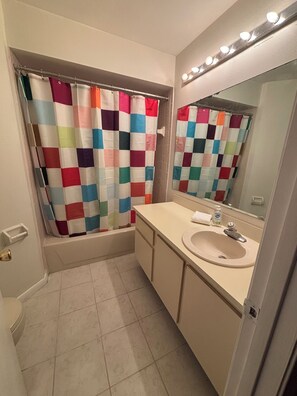 Un baño con cortina de ducha a cuadros, un lavamanos con espejo y una bañera.