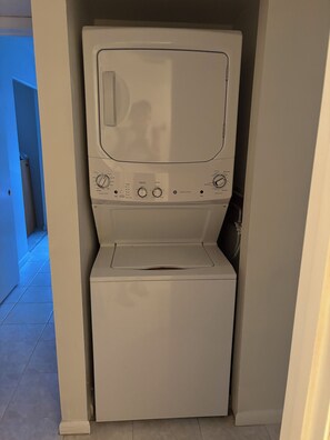 Un lave-linge blanc et compact, installé dans un espace étroit, doté de boutons de commande et d’une petite porte.