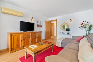 Un salon avec un meuble en bois, un téléviseur à écran plat, un tapis rouge et un canapé beige.