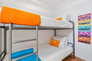 Un lit superposé avec une literie orange et bleue, des oreillers blancs et une affiche de voitures anciennes accrochée au mur.