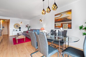 A modern living room with a glass dining table, grey upholstered chairs, a red rug, and a large abstract painting on the wall. - Panoramic Sea View by Albufeira Holidays (Albufeira)