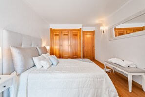 A bedroom with a large bed, a bedside table, a bench with towels, wooden wardrobes, and a mirror. - Panoramic Sea View by Albufeira Holidays (Albufeira)