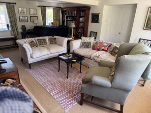A living room with a sofa, armchair, and a coffee table. There is a bookshelf and a window with curtains. - Cottage Sleeps 7 with Garden & Free Parking (Dorchester)