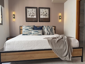 A bed with a quilted headboard, two wall-mounted light fixtures, and two framed floral artworks. - Vrbo Property (Santo Domingo)
