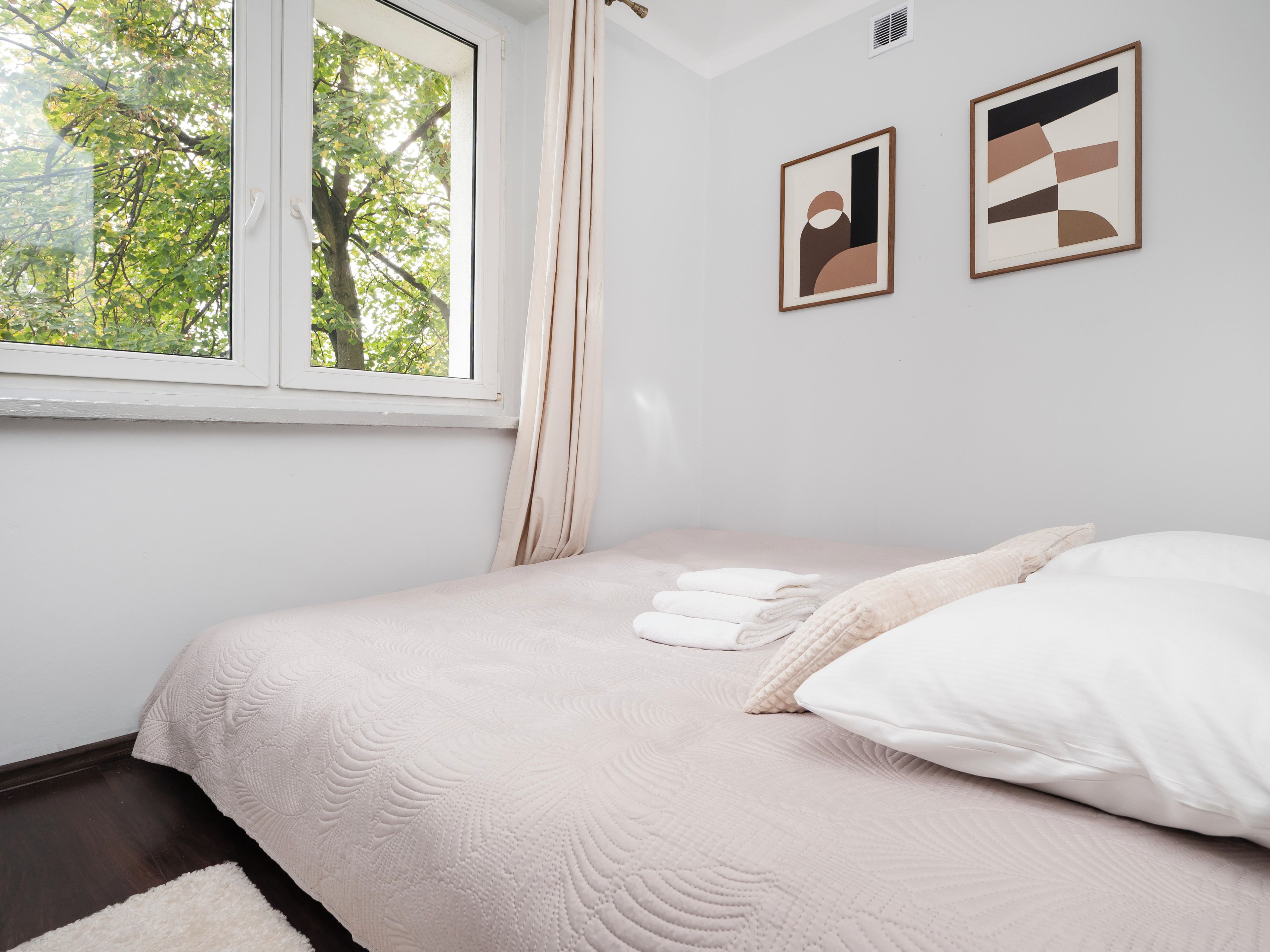 Quarto com cama, almofadas, janela e duas obras de arte emolduradas na parede.