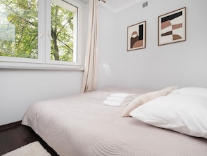 Quarto com cama, almofadas, janela e duas obras de arte emolduradas na parede.