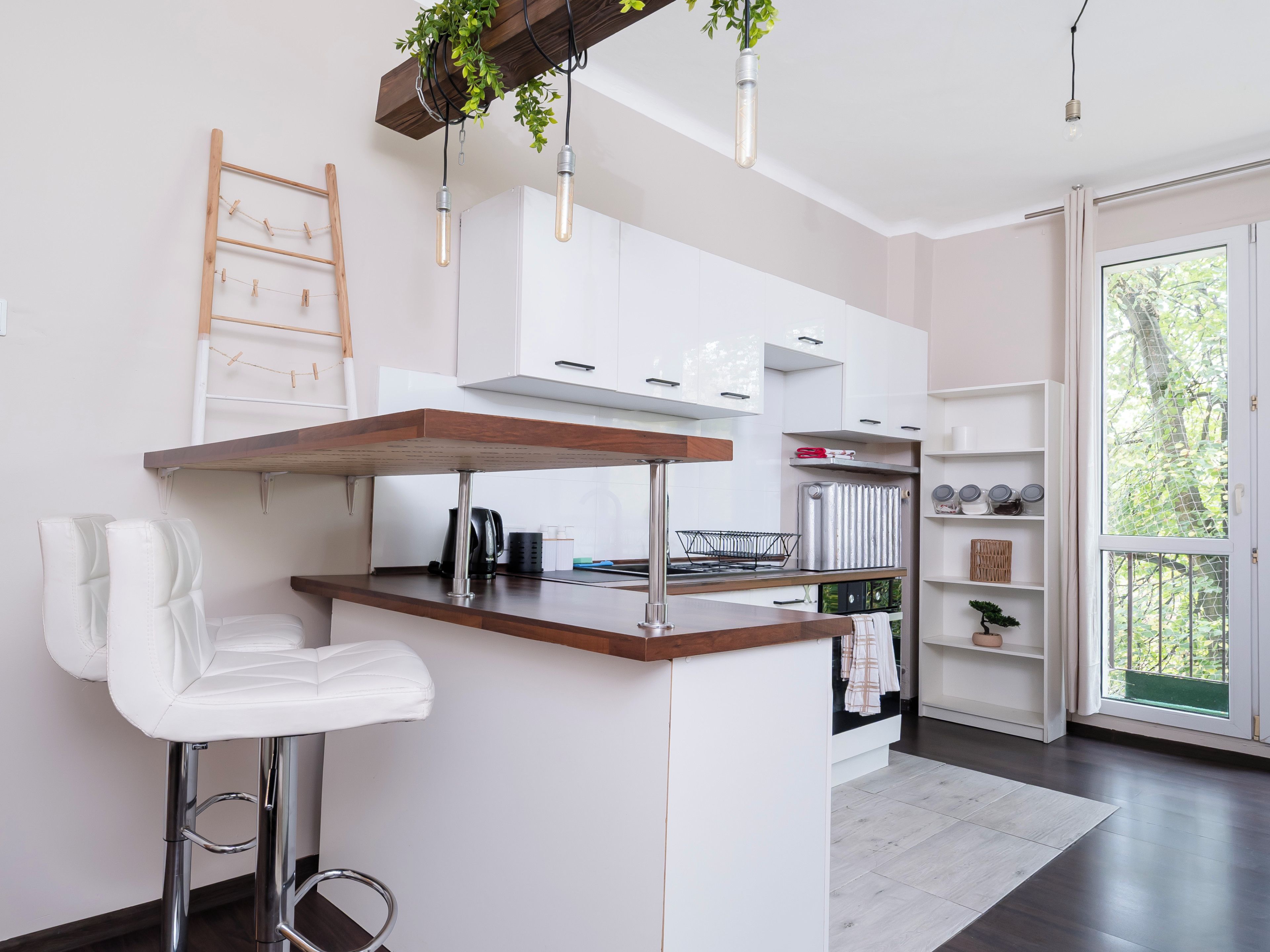 Cozinha moderna com ilha central, armários brancos e vista para o verde lá fora.