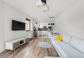 Een moderne woonkamer met een grijze bank, een klein rond tafeltje en een aan de muur bevestigde televisie.