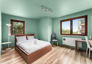A bedroom with a bed, a chair, a desk, a radiator, and a window with a view. - Park Reduta Harmony Apartment (Kraków)