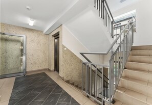 A modern interior with a staircase, elevator, and a glass door leading to a hallway. - Park Reduta Harmony Apartment (Kraków)