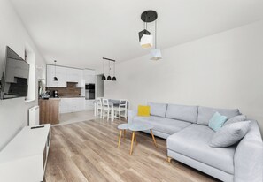 Een moderne woonkamer met een grijze bank, een kleine ronde tafel en een eethoek met een witte tafel en stoelen.