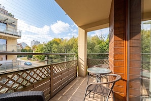 A balcony with a wooden railing, a glass safety barrier, and a small table with two chairs. - Park Reduta Harmony Apartment (Kraków)