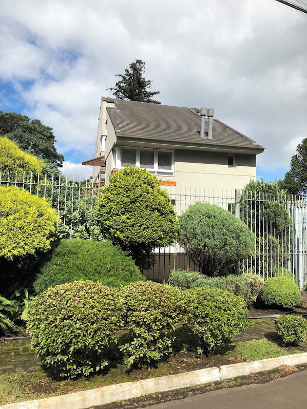 A residential building with a fenced garden area, surrounded by various shrubs and trees. - Vrbo Property (Gramado)
