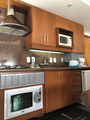 A kitchen with wooden cabinets, a microwave, a built-in oven, a range hood, and a stainless steel range. - Vrbo Property (Gramado)