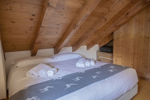 Una camera da letto con soffitto in legno, un letto con lenzuola bianche e una coperta grigia con motivi di renne.