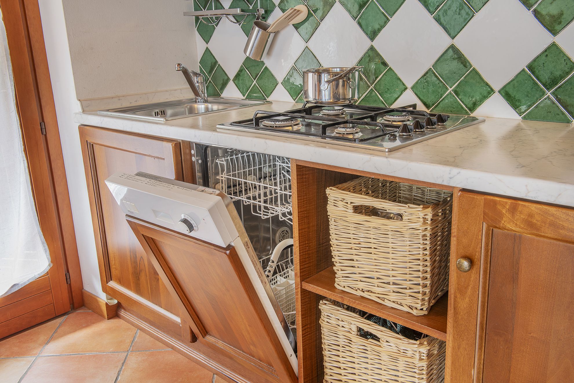 Una cucina compatta con lavastoviglie, fornello e cesti in vimini sugli scaffali.