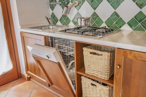 Una cucina compatta con lavastoviglie, fornello e cesti in vimini sugli scaffali.
