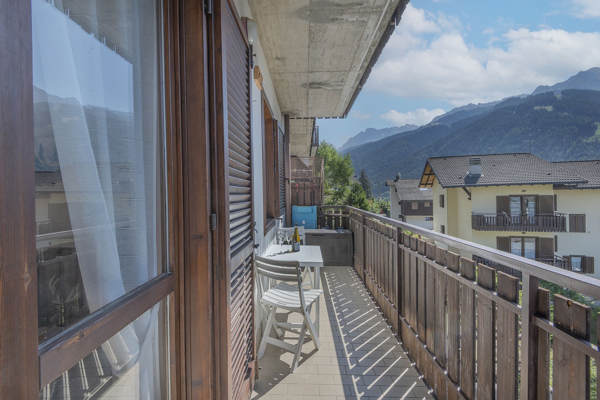 A balcony with a view of mountains, wooden railings, and a table with a bottle.
