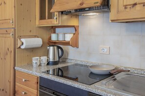 A kitchen with wooden cabinets, a stainless steel kettle, a coffee maker, and a built-in induction cooktop. - La Casa di Bud - AffittiPontediLegno (Temù)