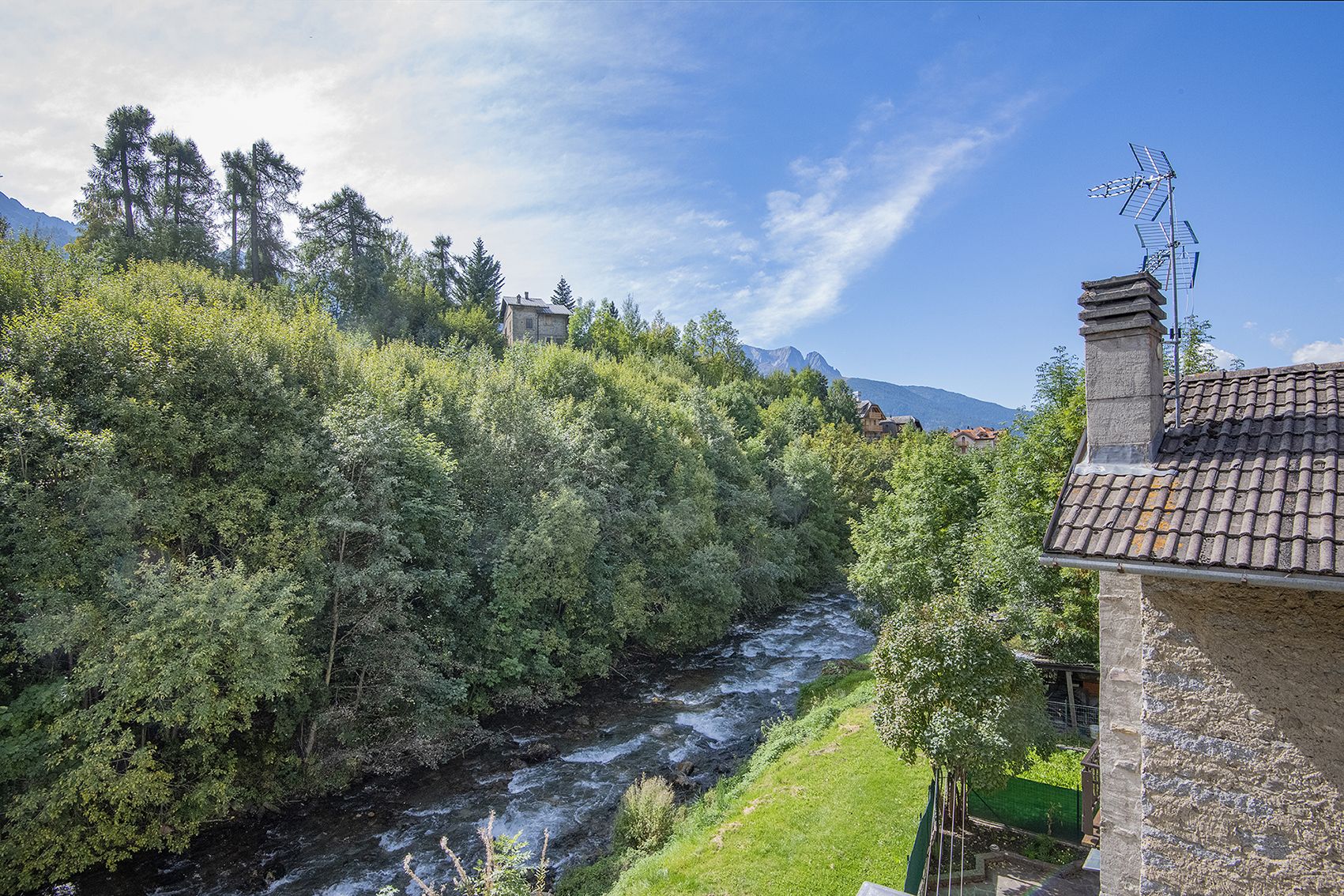 A river flowing through a forested area with houses on the right.