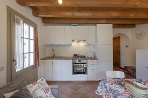 Cuina compacta amb armaris blancs, fogó de gas, forn i un rentamiques. Hi ha una zona de dinar amb taula i cadires.