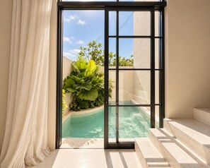 Een modern interieur met een glazen deur naar een zwembad, omringd door planten en een heldere lucht.