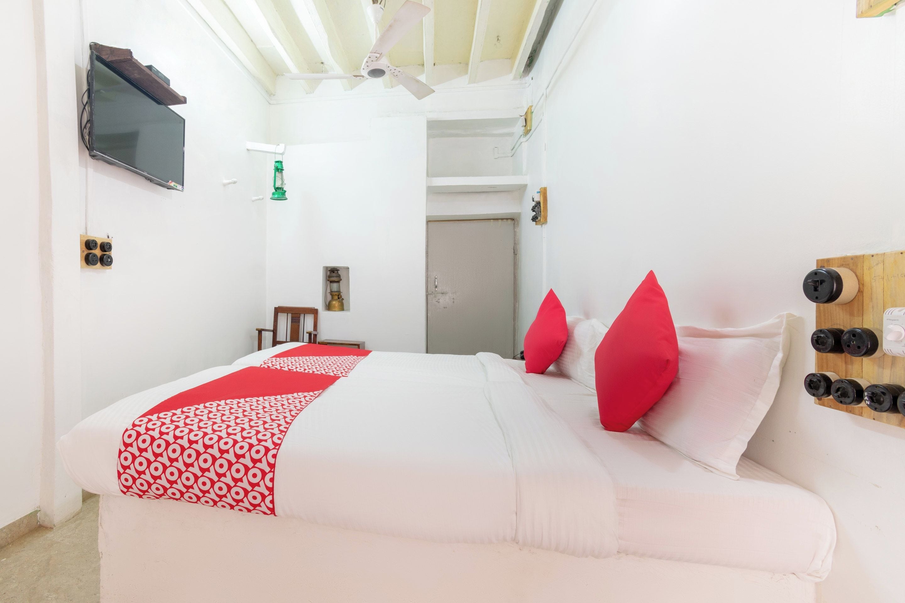Habitación de hotel con cama, televisor montado en la pared, ventilador de techo y panel de madera con botellas.