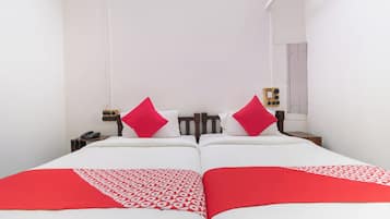 Una cama doble con dos almohadas, una mesita de noche con teléfono y un enchufe de pared.