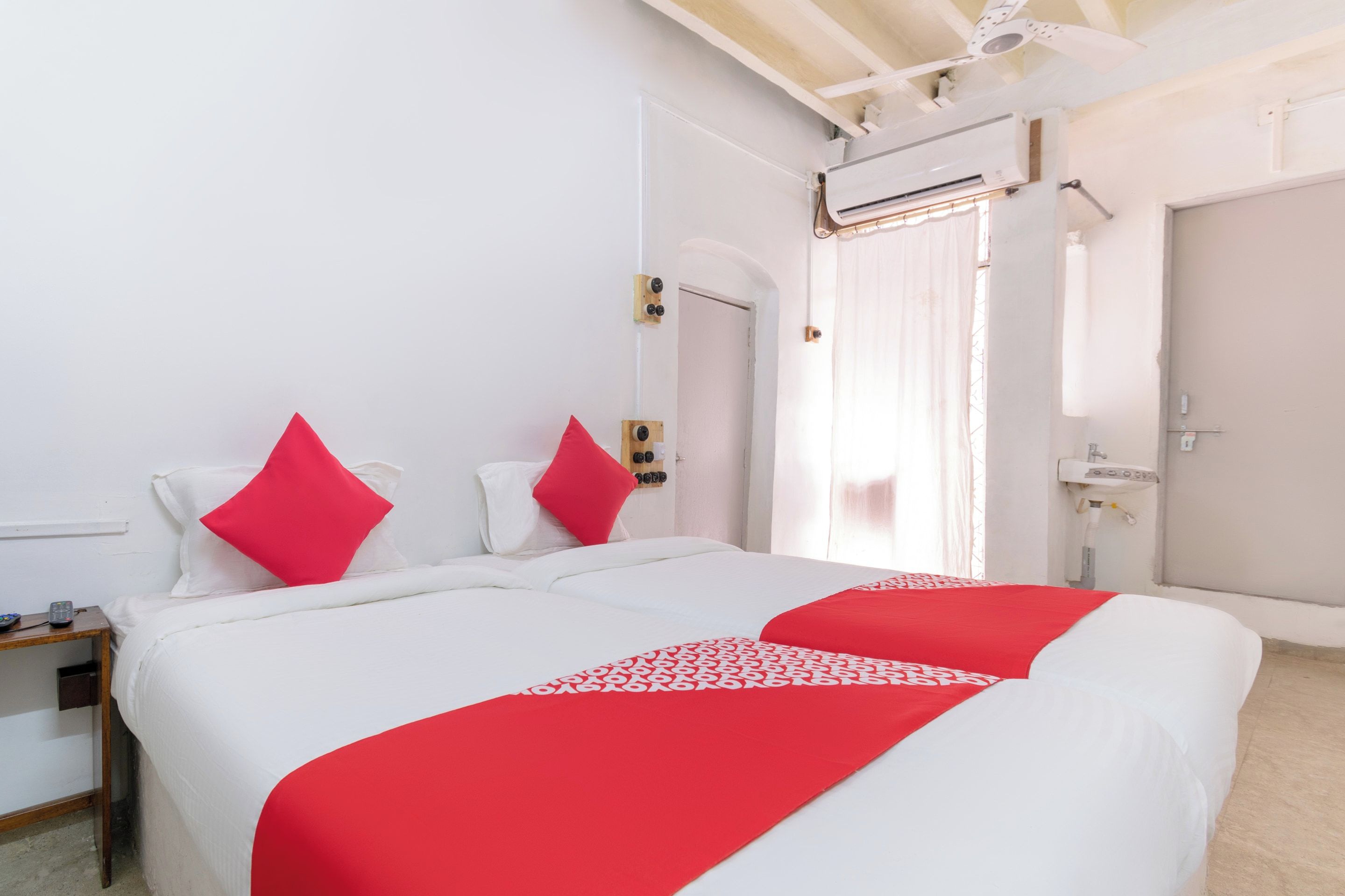Habitación de hotel con dos camas, una mesita de noche, un espejo, una ventana con cortinas y un ventilador de techo.