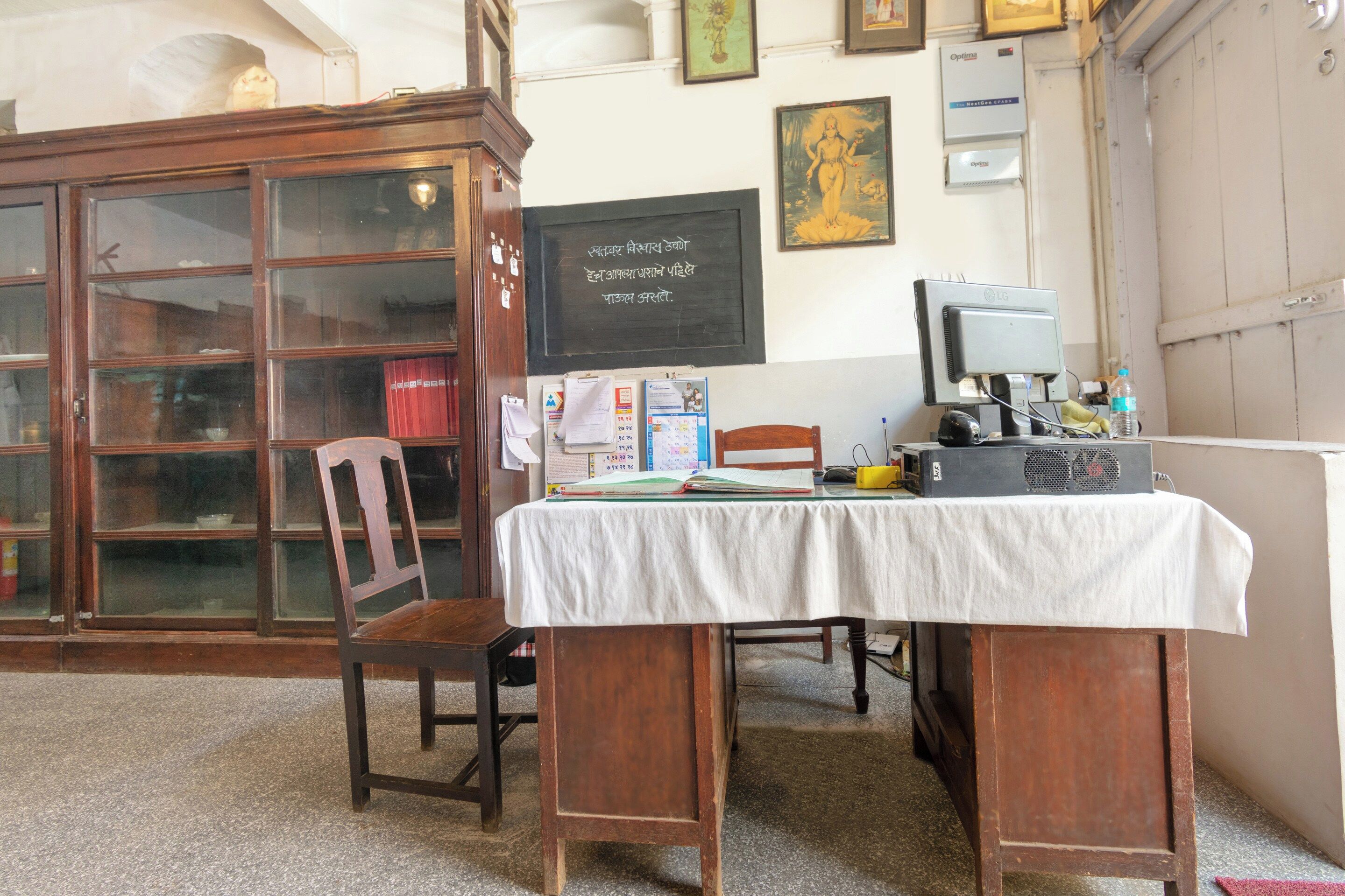 A room with a wooden desk, a chair, a bookshelf, and a chalkboard with writing.