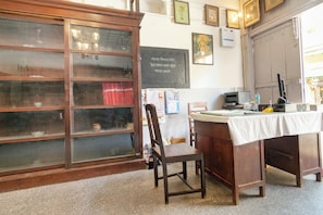 Una habitació amb un armari de fusta amb portes de vidre, un escriptori amb un ordinador i una cadira. Hi ha quadres emmarcats a la paret i una pissarra amb text.