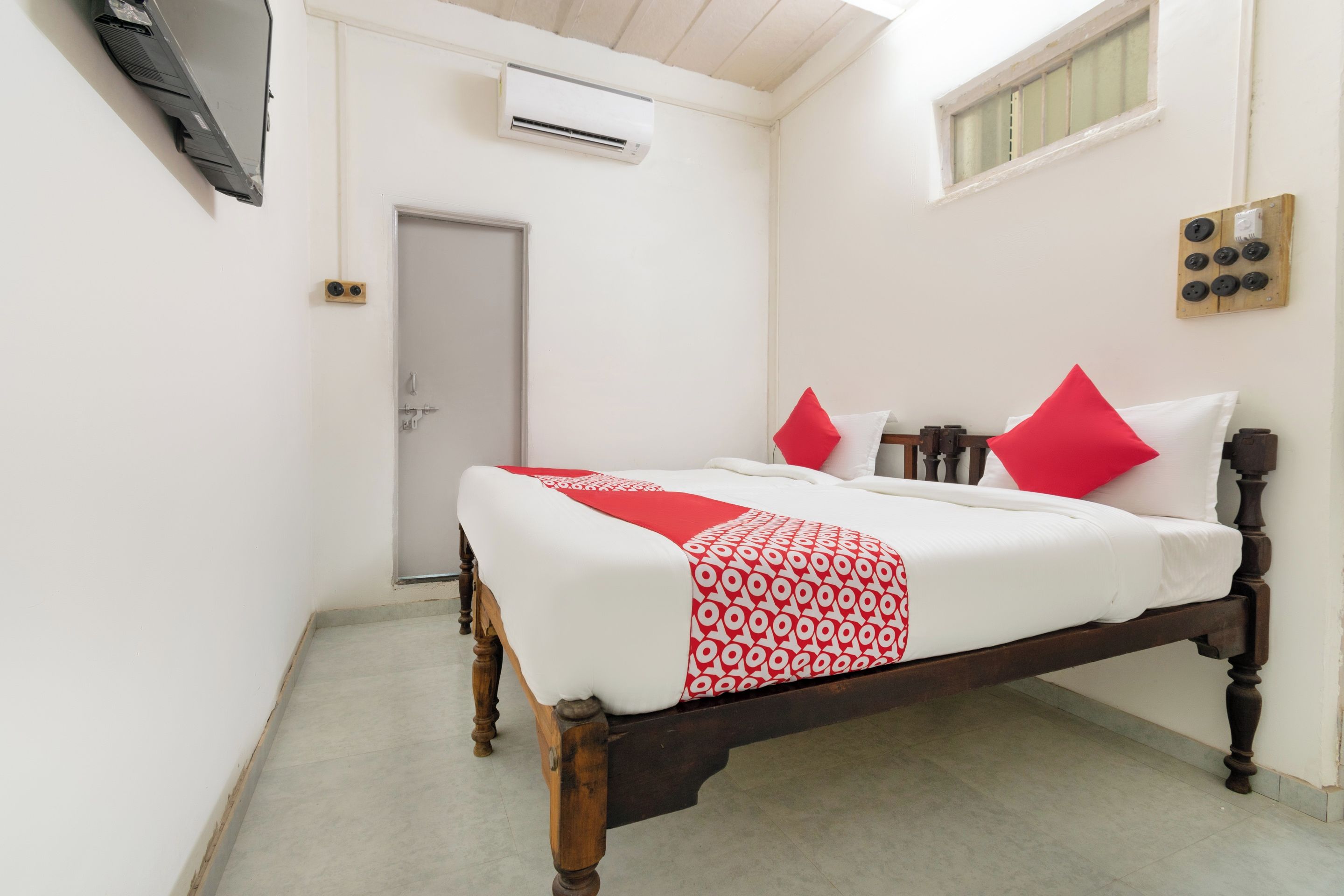 A bedroom with a wooden bed, white walls, a door, and an air conditioning unit.