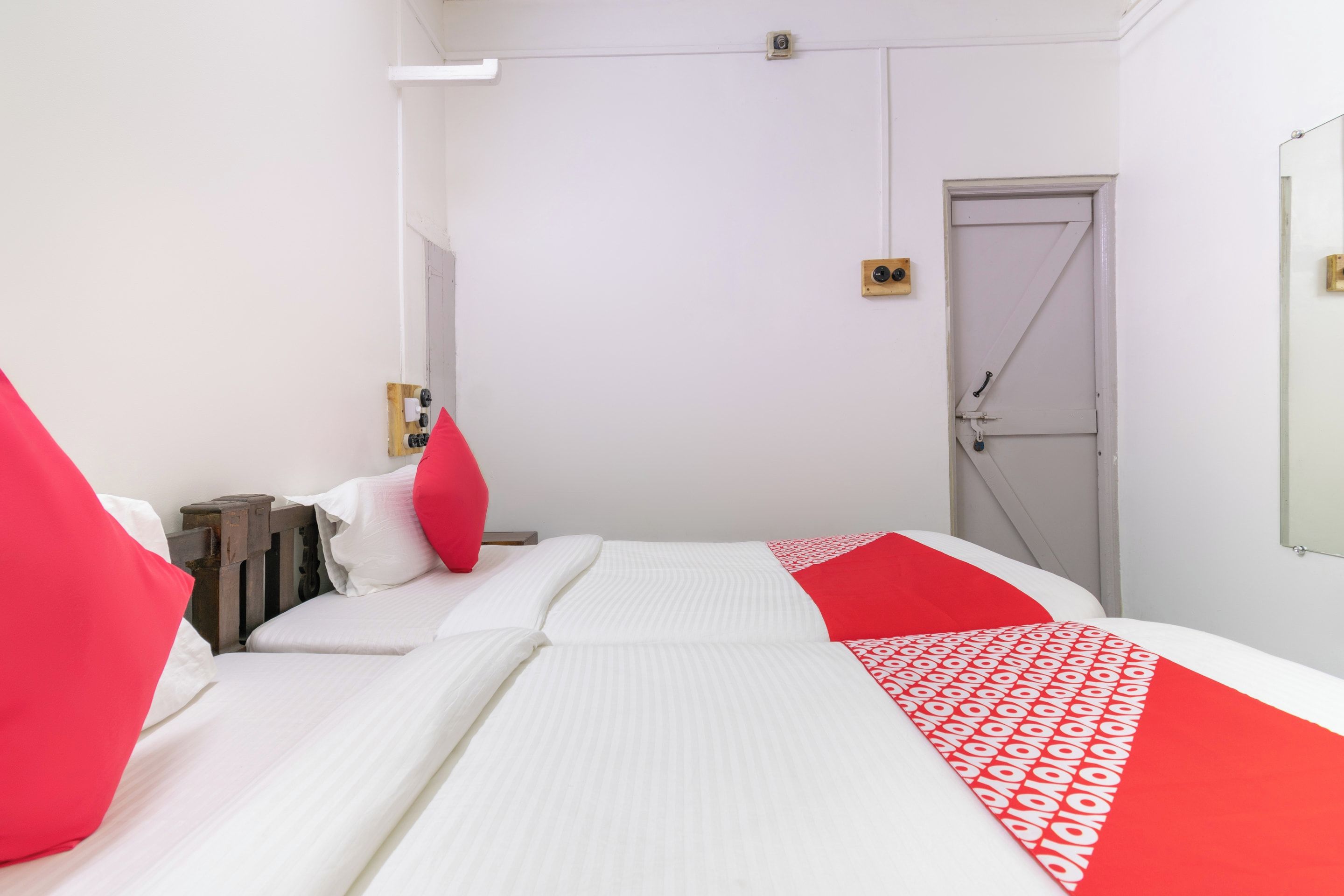 A hotel room with a bed, a door, and a small wooden nightstand.