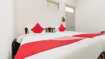 Una cama con ropa de cama blanca y detalles rojos, un cabecero de madera, una mesita de noche con una lámpara y una puerta con un ventanal encima.