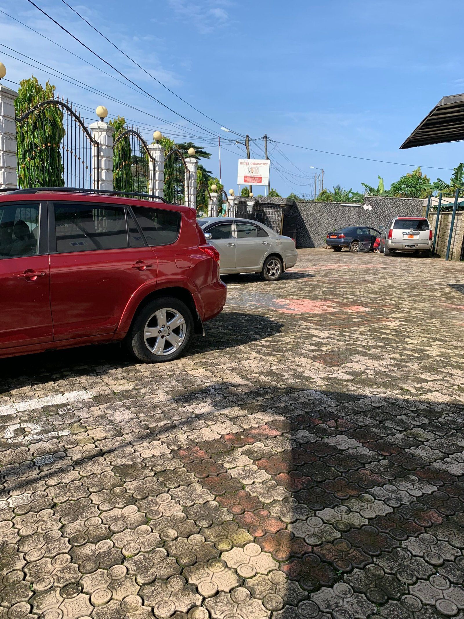 Un estacionamiento pavimentado con varios automóviles, un letrero de hotel y una entrada porticada con detalles decorativos.